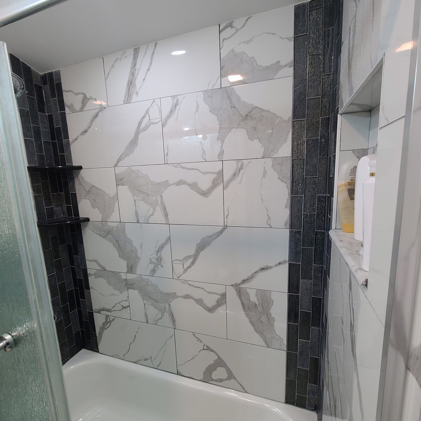 Tiled tub surround with marble-look panels and dark accent tile